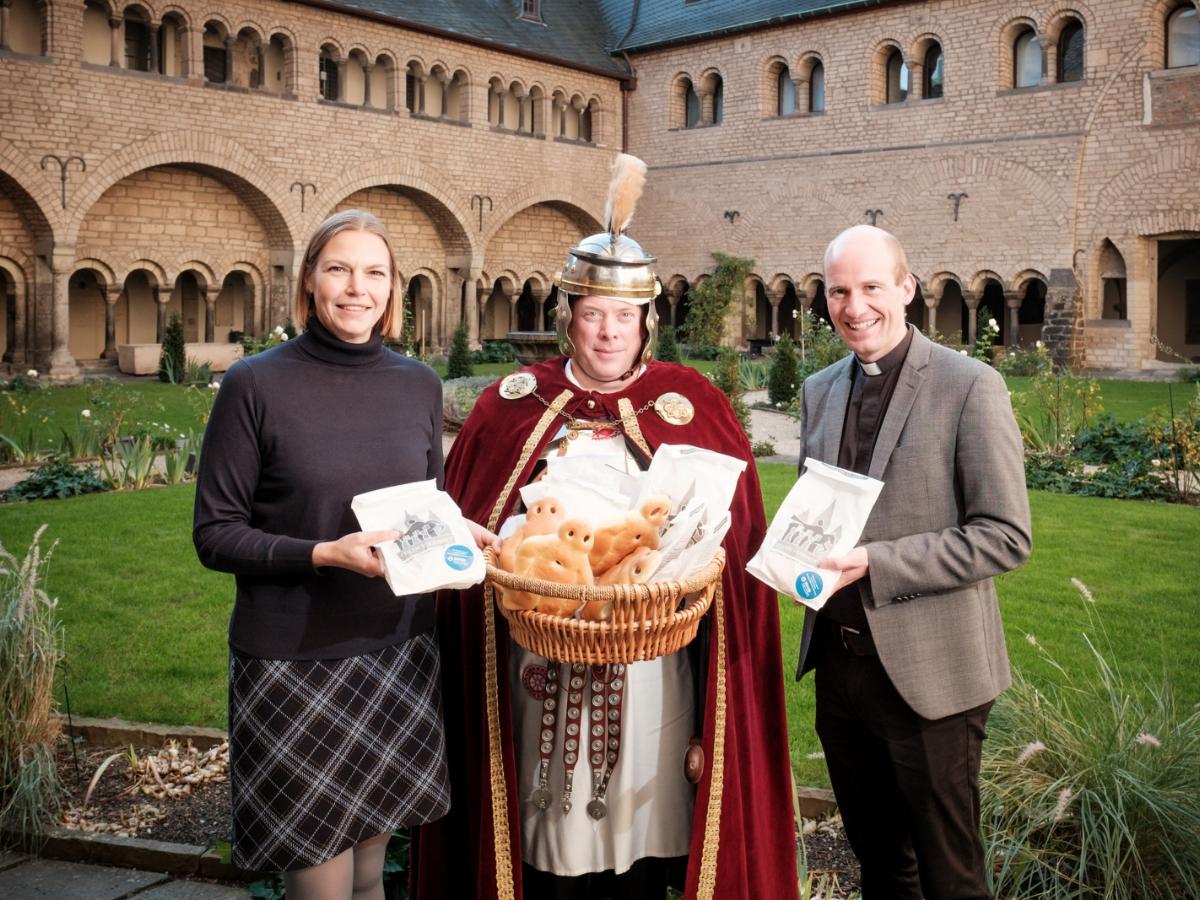 Lisa Pias, Fachbereichsleiterin Marketing: Strategie und Digitales bei den Stadtwerken Bonn und Münsterkaplan und Pfarrverweser Dr. Christian Jasper gemeinsam mit dem „St. Martin“ (Martin Heide) bei der symbolischen Übergabe der Weckmänner im Kreuzgang der Bonner Münsterbasilika.