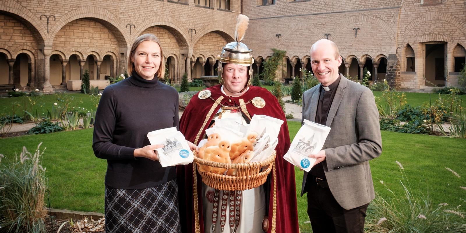 Lisa Pias, Fachbereichsleiterin Marketing: Strategie und Digitales bei den Stadtwerken Bonn und Münsterkaplan und Pfarrverweser Dr. Christian Jasper gemeinsam mit dem „St. Martin“ (Martin Heide) bei der symbolischen Übergabe der Weckmänner im Kreuzgang der Bonner Münsterbasilika.